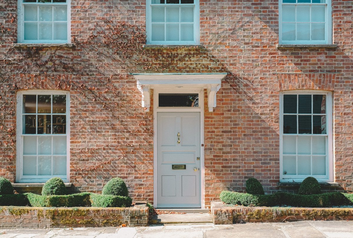 Bakstenen woning met een witte voordeur en schuiframen met kleine ruiten