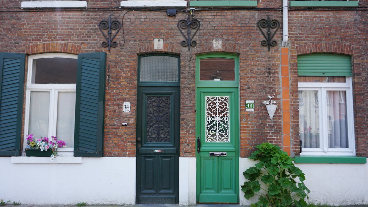 Bakstenen gevel met een groene voordeur, een zwarte deur en witte ramen met luiken